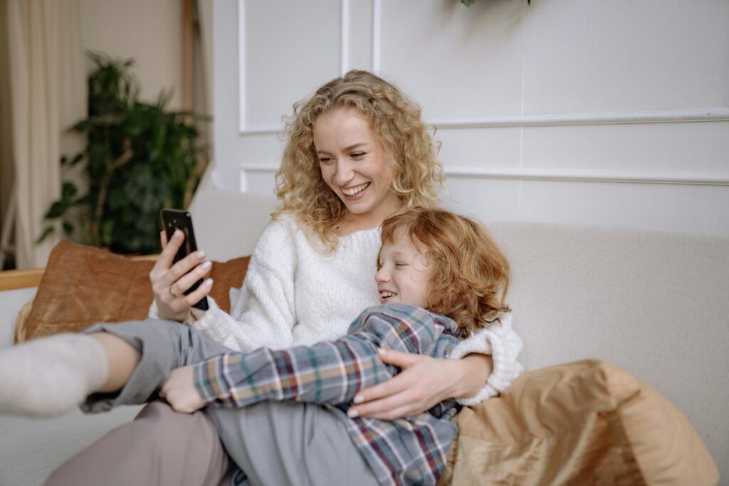 A joyful mother and son taking a selfie together while lounging on a couch indoors.